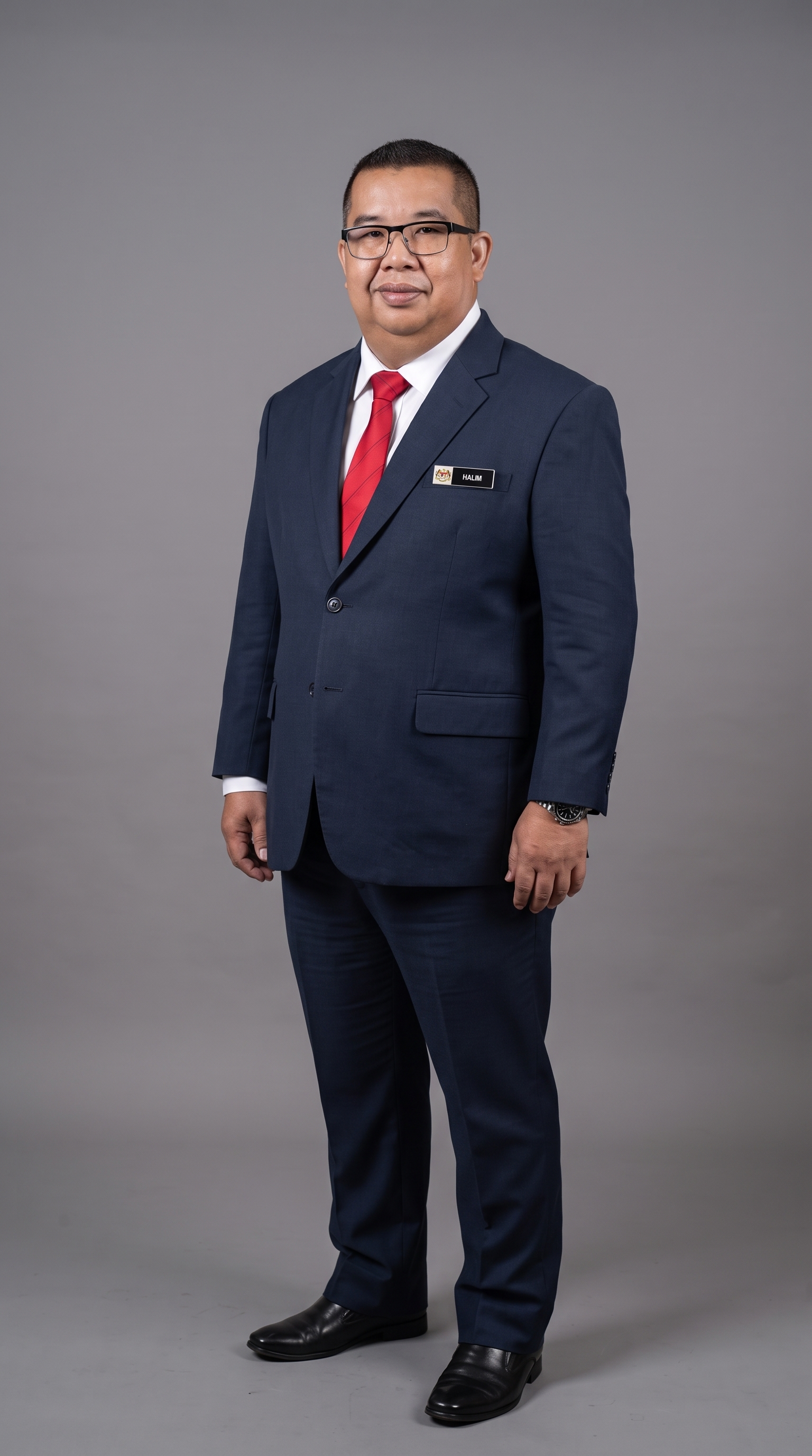 Halim bin Omar, Pegawai Pendidikan Daerah Kuala Selangor, mengenakan sut biru navy dan tali leher merah.